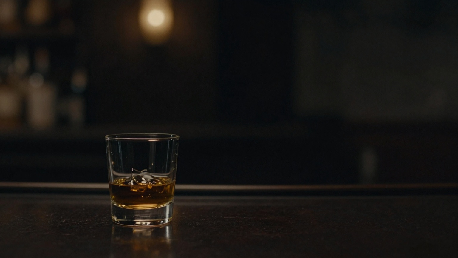 Szklanka whisky na ciemnym barze, w tle rozmyte ciepłe światła - obraz patrzenia z dystansu, gdy była jest z kimś nowym